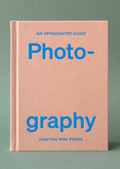 A pink hardcover book with blue lettering titled "An Opinionated Guide To Photography".