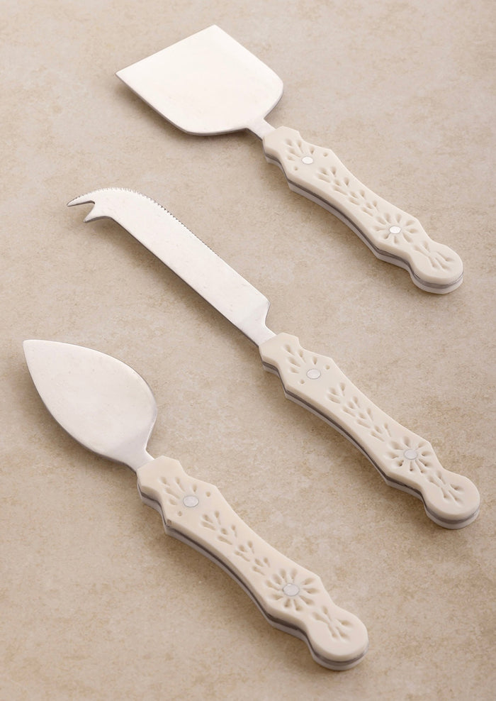 Three different cheese knife styles in silver with eyelet detailed cream resin handles.