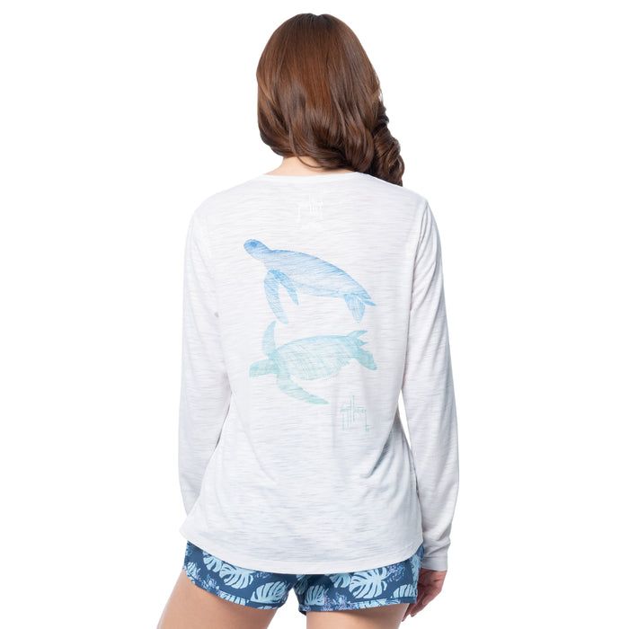 Woman wearing a white long-sleeve shirt with a turtle design on the back, standing against a white background.