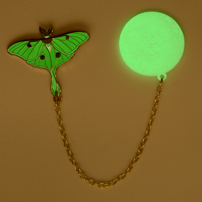 Moth and moon pins glowing green in dimmed light.