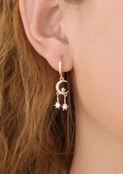 A pair of gold and clear crystal earrings with huggie hoop and moon and star crystal dangle charm.