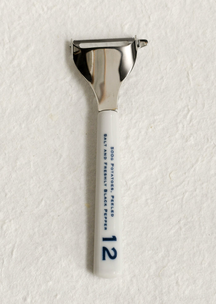 A vegetable peeler with ceramic white and blue handle with blue text.