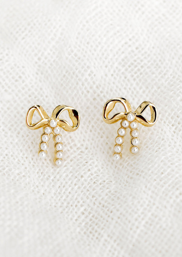 A pair of gold bow studs with tiny pearl detailing on "strings".