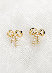 A pair of gold bow studs with tiny pearl detailing on "strings".
