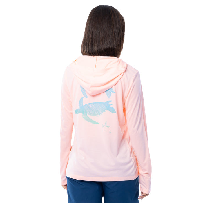 Person wearing a light pink hoodie with a turtle design on the back, standing against a white background.