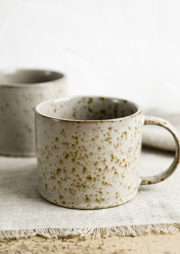 A brown speckled coffee mug with round handle.