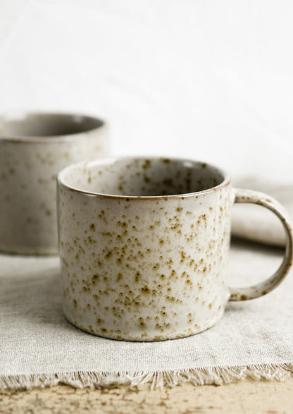 A brown speckled coffee mug with round handle.