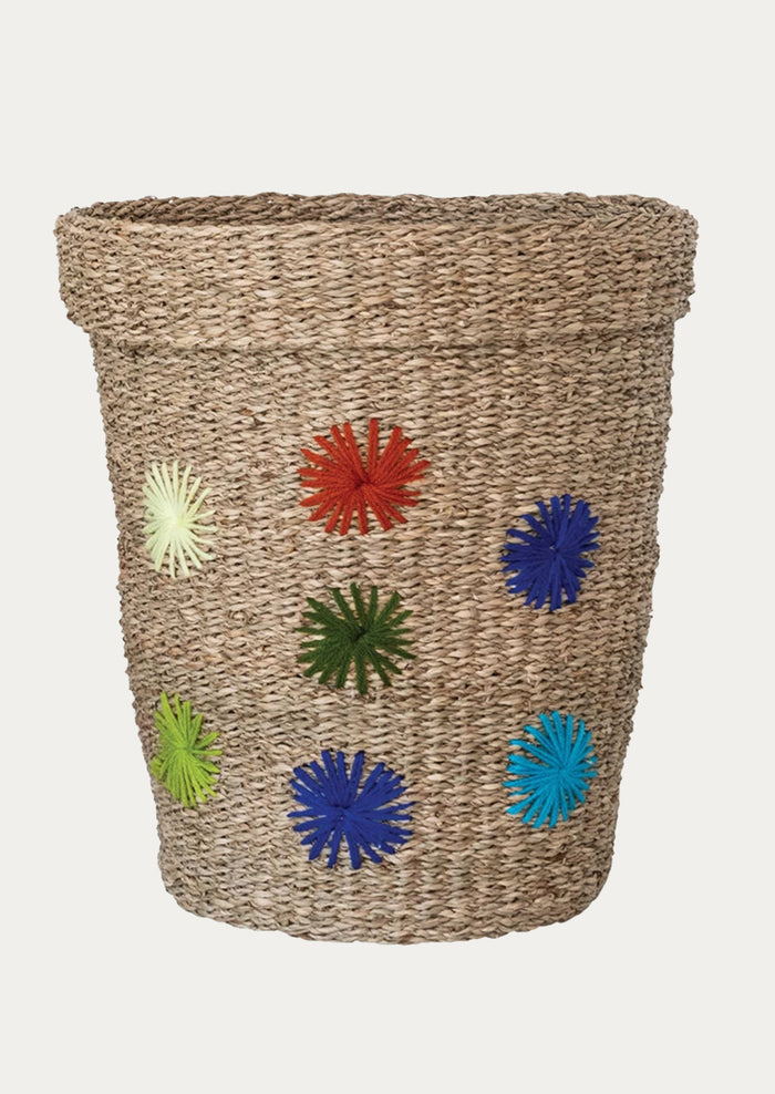 A natural seagrass storage basket with multicolor embroidered wool starburst pattern.