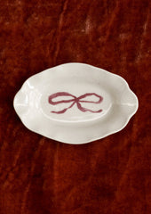 A small porcelain dish with ornate shape and hand painted bow illustration in red.