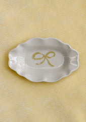 A small porcelain dish with ornate shape and hand painted bow illustration in yellow.